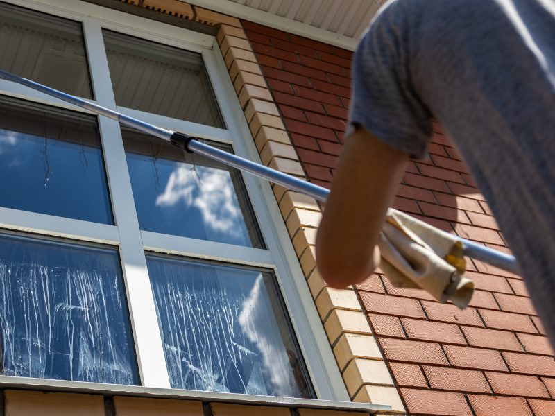 Man washing tall house window with cleaning tool