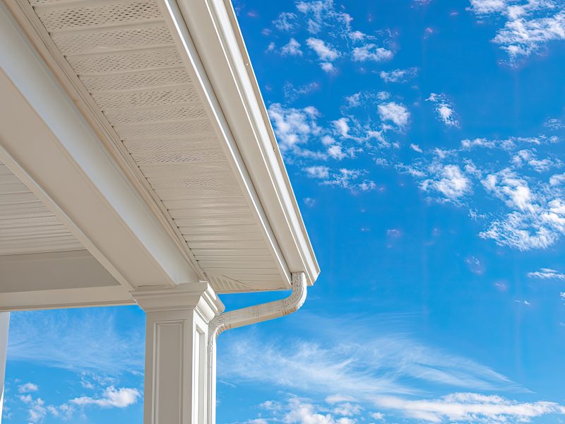 Close up of a house gutter system against a bright blue sky.